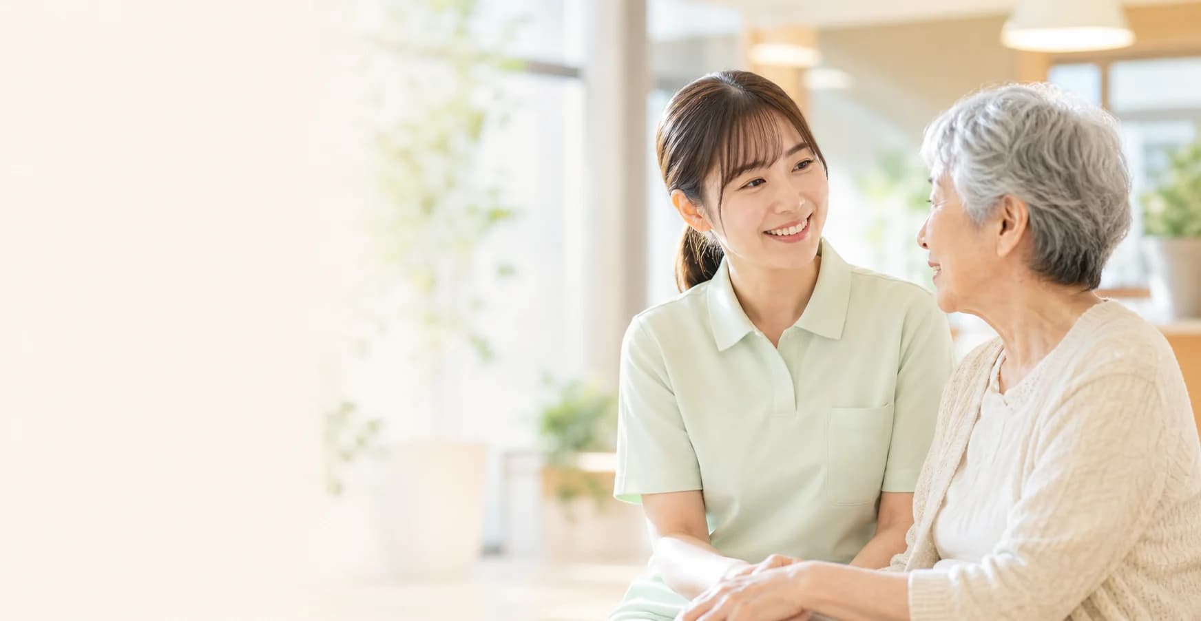 明るい介護施設で笑顔で会話する介護職員と高齢の女性